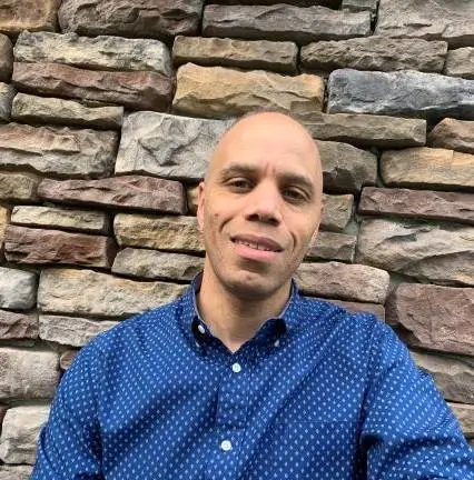 Man smiling in blue shirt against stone wall