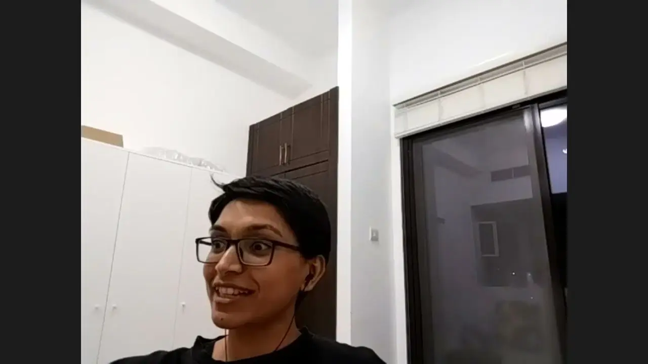 Smiling person with glasses and earbuds indoors