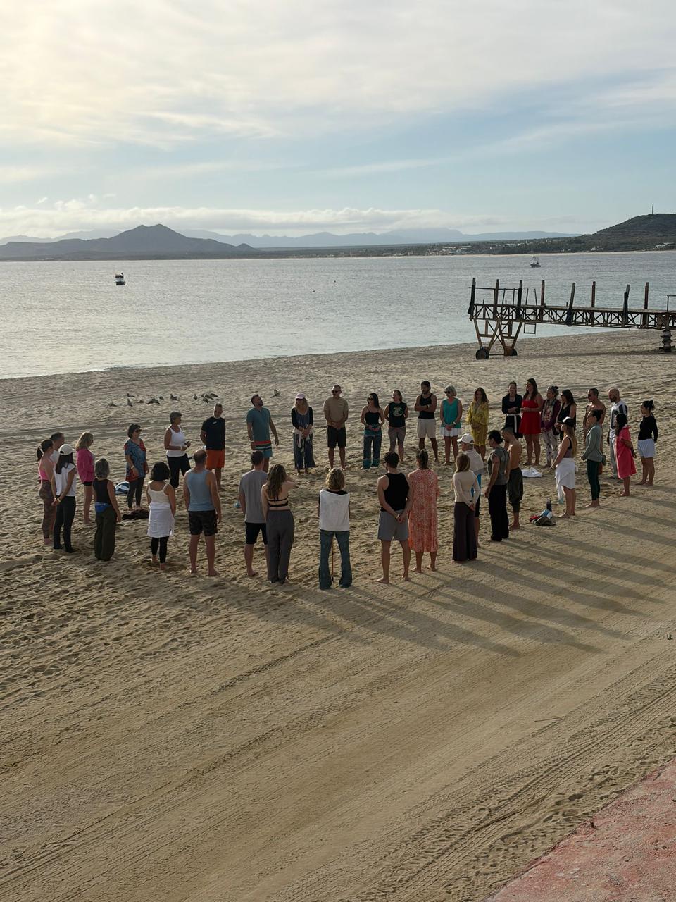 Group forming circle on beach near pier